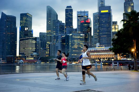 Singapore, Republic of Singapore - May 3, 2011: People running in the evening on embankment in front of business center. Running is very popular sports in Singapore