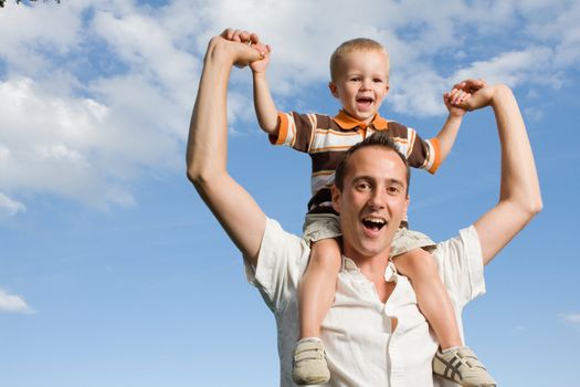Father carrying his son on piggy back ride outdoors against nature and blue sky