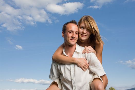 Two young lovers holding each other piggy back against blue sky and nature