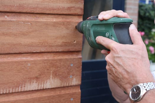 Man working with a power drill on a wooden construction