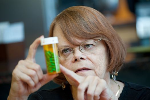 Senior woman examining prescription bottle with green capsules