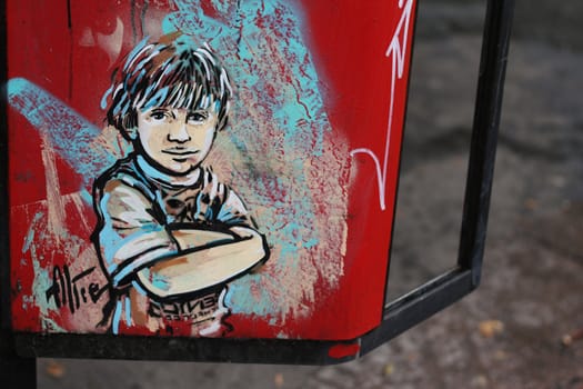A street art piece painted on a phone booth depicting a kid crossing his arms.