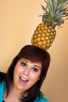 A young woman with a funny expression balancing a pineapple on her head.