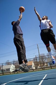 A young basketball player shooting the basketball and his opponent trying to block it.