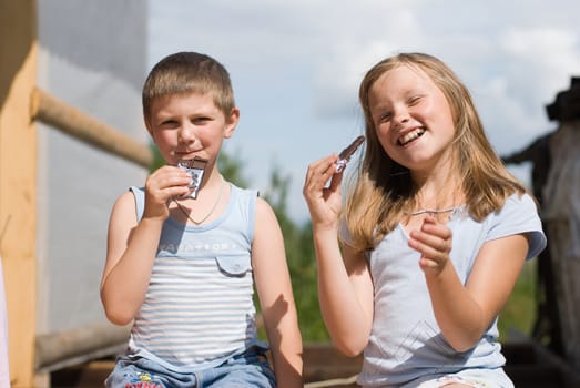 The brother and sister on summer vacations eat chocolate.  A warm sunny day in village