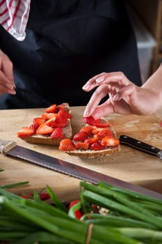 Hands putting strawberries on a wholeweat sandwich