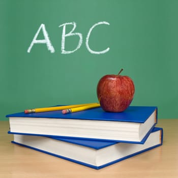 ABC written on a chalkboard. Books, pencils and an apple on foreground.