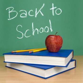 Back to school written on a chalkboard. Books, pencils and an apple on foreground.