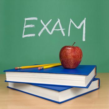 Exam written on a chalkboard. Books, pencils and an apple on foreground.