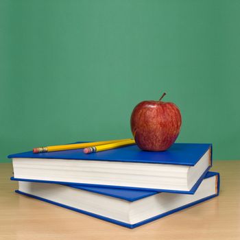 Blank chalkboard. Books, pencils and an apple on foreground.