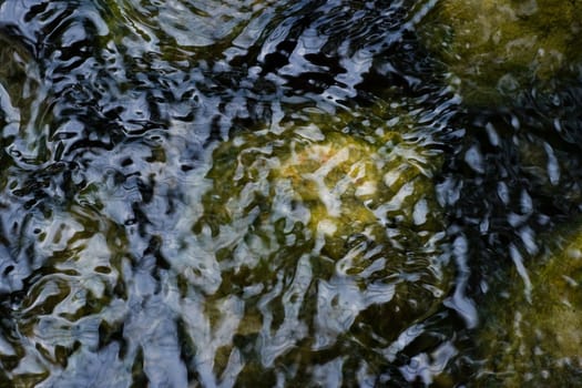 Boulders under and ripples in surface of water 