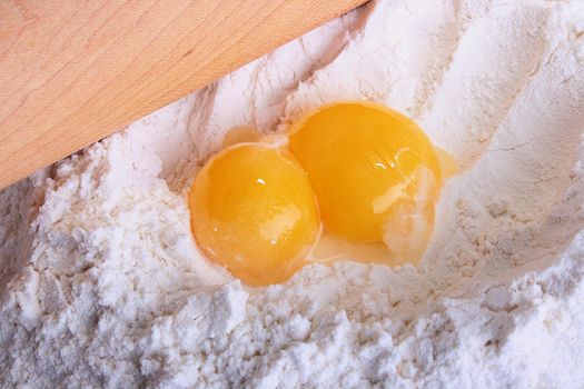 Two yolks lie on a flour with rolling pin. The pie beginning.