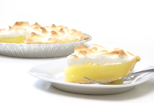 A slice of lemon meringue pie with the whole pie in the background.
