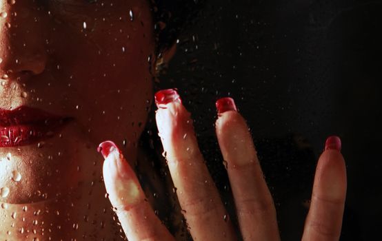 Female hand behind wet glass