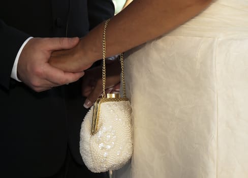 An intricately designed bride's purse with couple's hands in the background