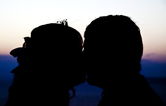 A newly wed couple kissing and silhouetted against Mediterranean sky