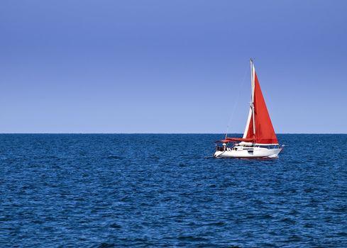 Yacht with a red sail offering crisp contrast against sky and ocean blue