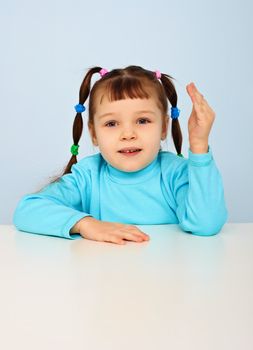 Little girl sitting at school desk on blue background