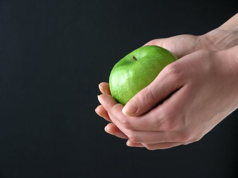 Green Apple in hands on black background
