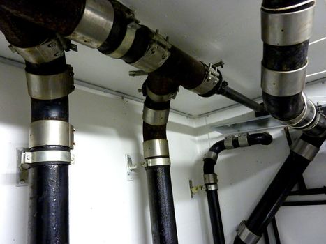 Several crossing black pipes with metal against white wall