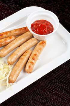 Grilled sausages with cabbage, greens and tomato sauce on white plate
