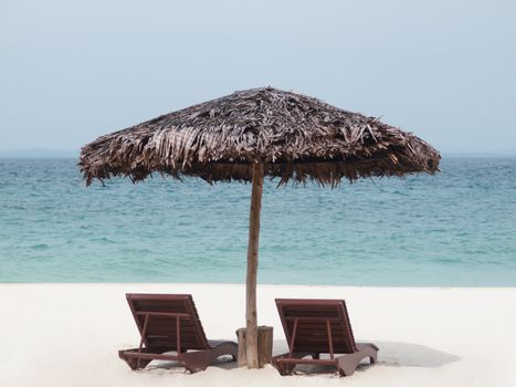 Two empty chair and an umbrella on the beach resort facing the south China sea in Pulau Besar Malaysia with a boat in the background