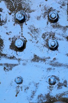 Screws, bolts and nuts on a very old iron crane. The blue paint is not completely covering anymore, so the dark iron underneath it partially becomes visible. Grungy background image.