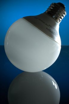 A CFL globe lamp, standing with its base pointing upward, on a dark reflective surface with a blue illuminated background.