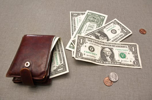 Wallet with dollar bill sticking out, and a fan of four dollar bills beside it, plus a few scattered coins, all on a gray backdrop.