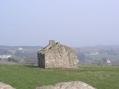 An old stone cottage stands derelict in a field.