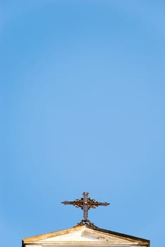 A Baroque cross on top of a church (not visible in the shot) with blue sky as the background.