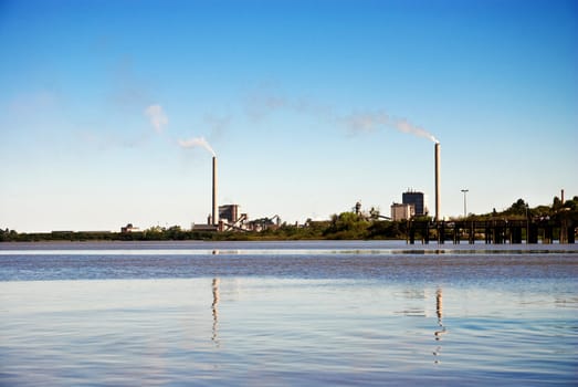 Lake and blue sky with two factory chimneys far away emitting fumes.