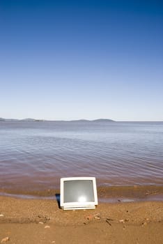 A computer monitor in the sand, with blue sky. Coastline shot.