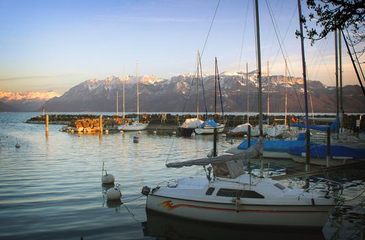 A Marina showing various boats against a background of lake Geneva and the Alps.