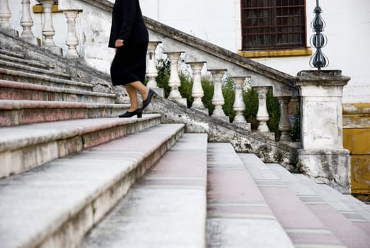 Black dressed female figure climbing up an old staircase. Shot is sideways.