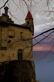 Image of partial castle on left with yelllow sky, clouds, mountains and Lake Geneva.