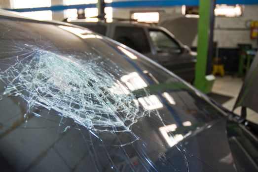 Detail shot of a shattered car windshield in a repair shop.