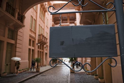 Dark wooden sign board with pink Victorian building in the background. Low angle shot.