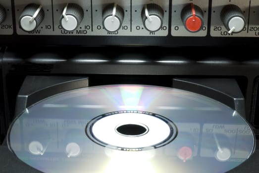 Detail shot of a CD in a player's drawer with crossover buttons on top. Front shot with dark background.