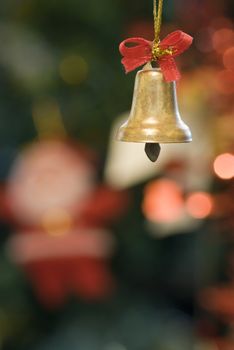 Decorative xmas bell with red ribbon with blurred xmas tree decoration in the background.