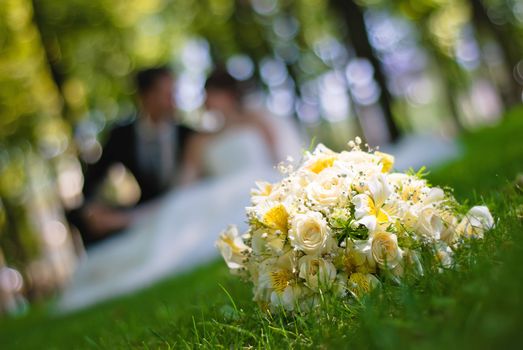 bridal bouquet of white roses on a green meadow and blurred newlyweds