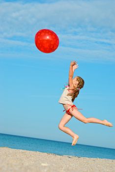 Jumping little girl with red ball on the beach