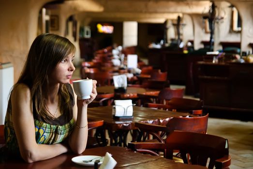 Beautiful young woman sitting in an empty cafe with a cup of coffee