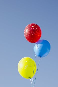 Three balloons tied with strings. Multicolor balloons red blue and yellow with painted hearts.