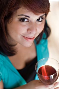 A happy young woman holding a glass of red wine.  Shallow depth of field with focus on the eyes.
