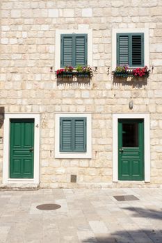 Three windows with shutters and two green wooden doors.