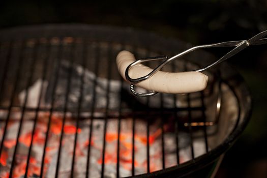 white sausage held by barbecue tongs over a grill