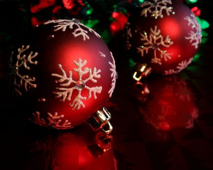 Two red christmas baubles illuminated on glossy red paper.
