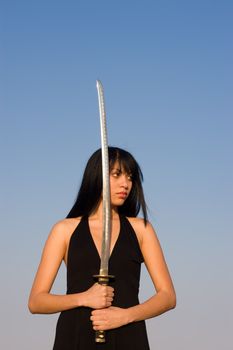 Asian model posing with a Samurai sword against blue sky