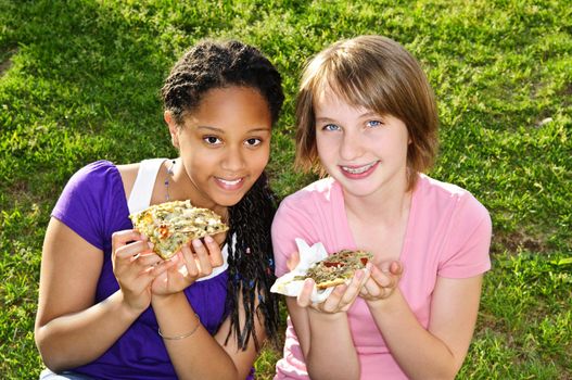 Two teenage girls sitting and eating pizza